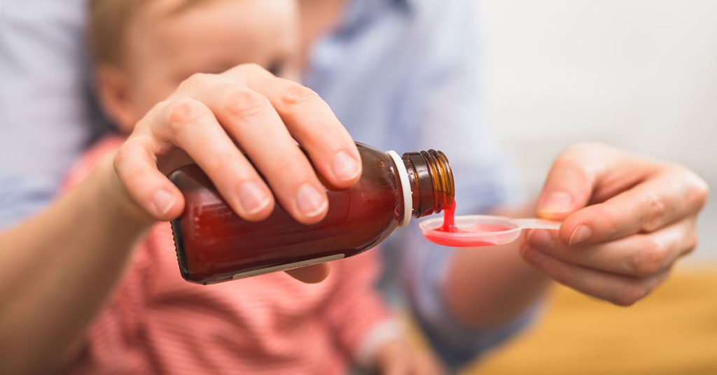 close up of mother pouring cough syrup. blurred baby boy in back